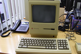 Macintosh Plusとキーボードが電話などと一緒にオフィスの机に置いてある様子。